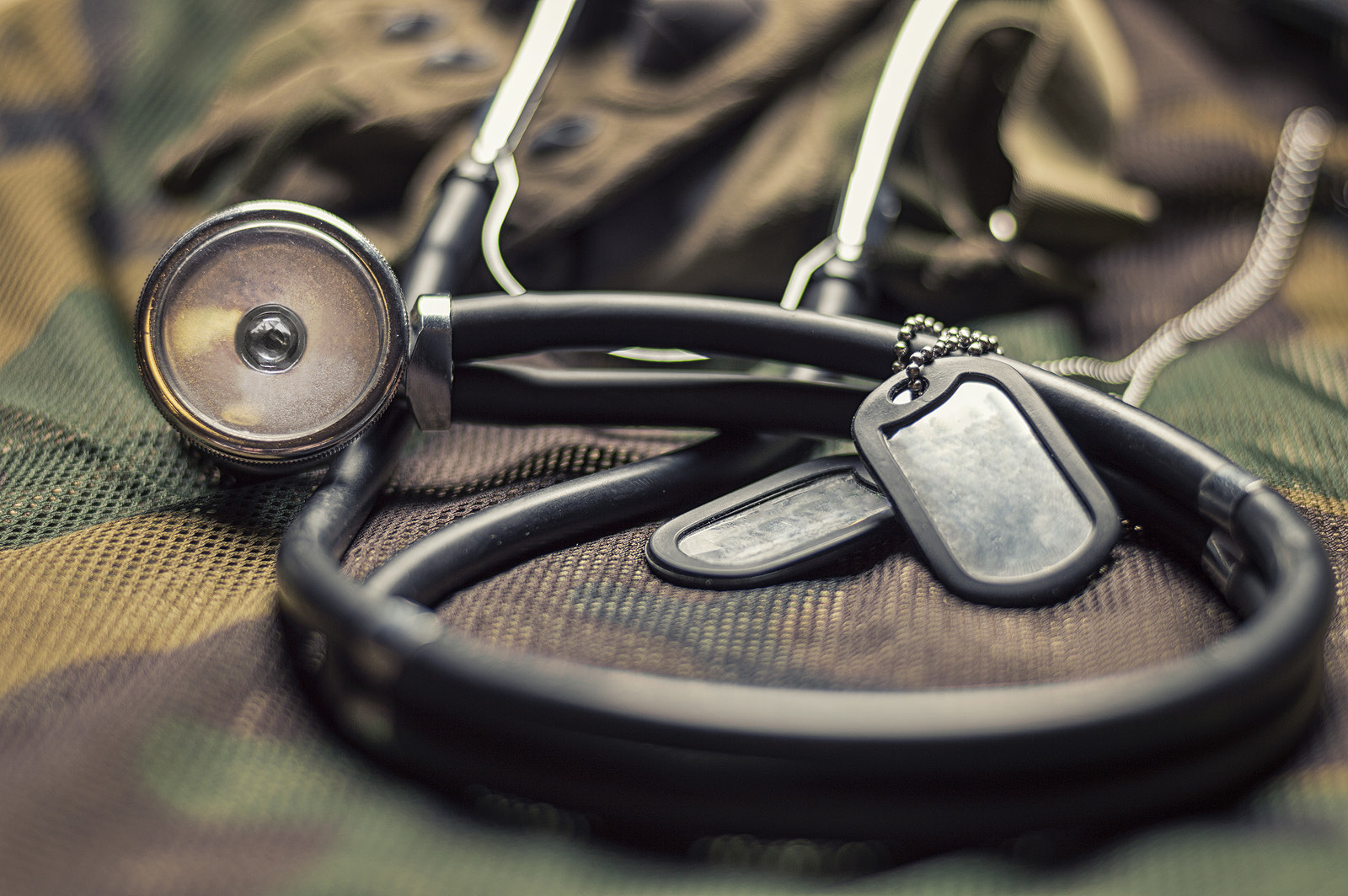 A stethoscope and military dog tags resting on a camouflage uniform